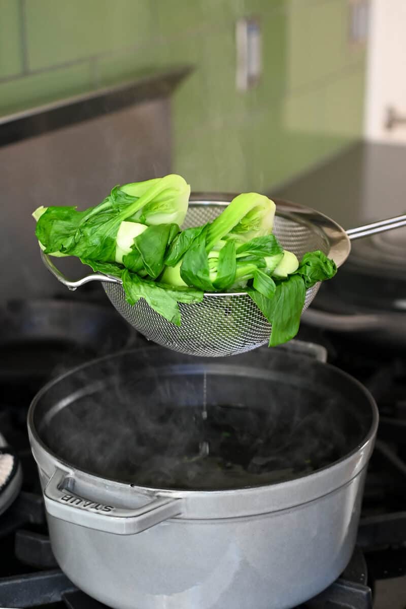 Removing some blanched baby bok choy from a pot of boiling water.