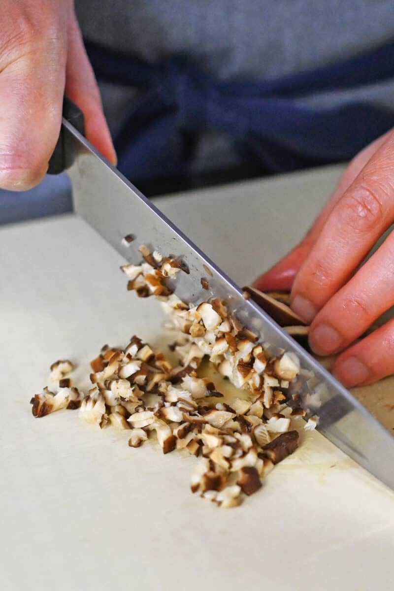 Closeup of someone finely chopping rehydrated dried shiitake mushrooms on a cutting board.