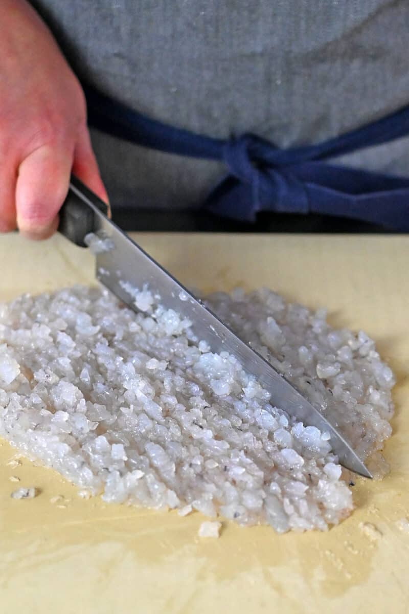 Raw shrimp is chopped into a fine paste on a cutting board with a chef's knife