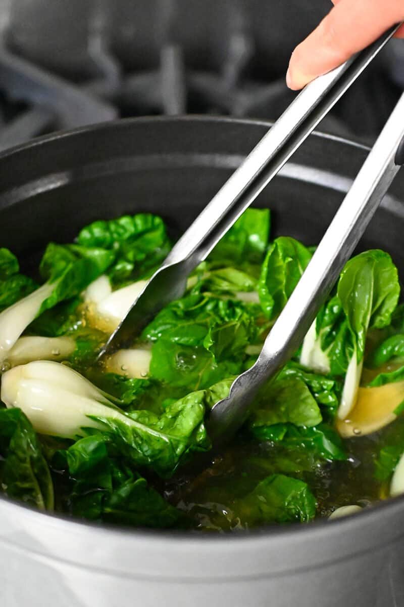Adding baby Bok Choy to a pot of simmering chicken broth