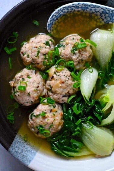An overhead shot of a bowl with wonton meatballs and baby Bok Choy in a bowl of clear broth.