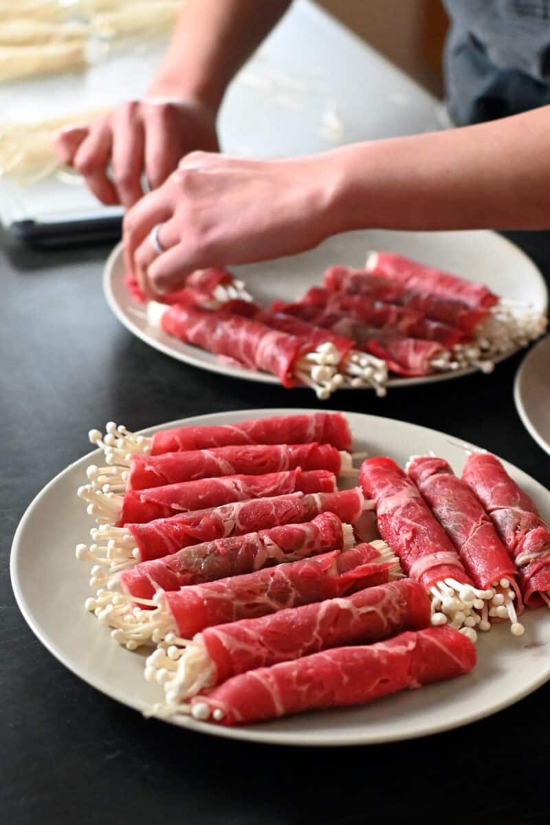 Two plates filled with beef and enoki mushroom rolls ready to be cooked.