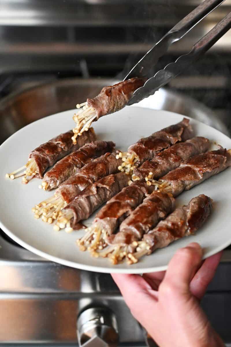 Placing cooked beef and enoki mushrooms on a white plate.