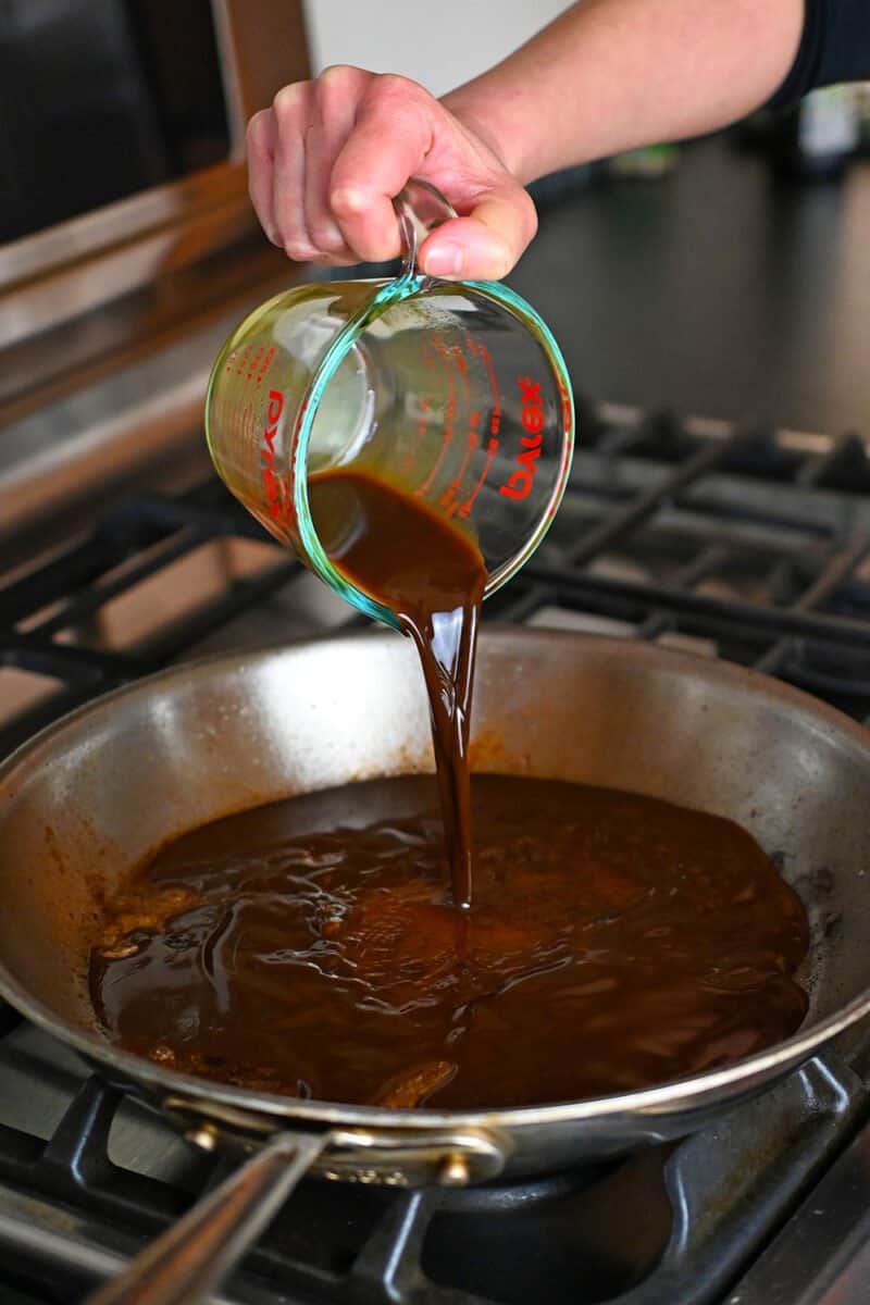 Pouring All-Purpose Stir-Fry sauce into a large stainless steel skillet.
