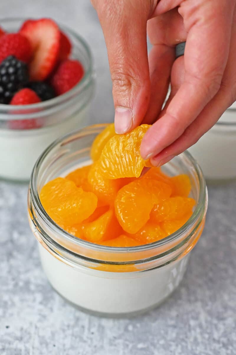 Photo of a hand placing peeled orange segments onto a jar of coconut jelly dessert
