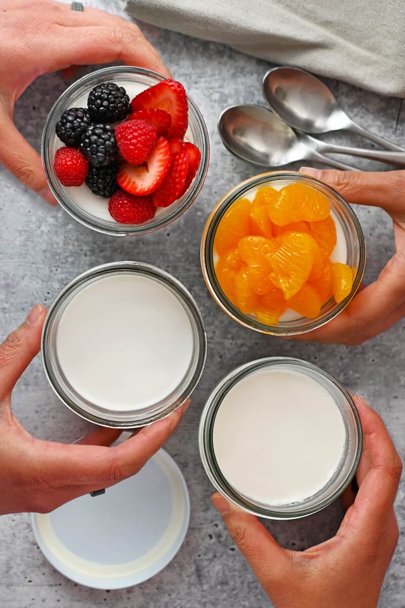 An overhead shot of four jars filled with coconut jelly desserts, two are topped with mandarin oranges or fresh berries.