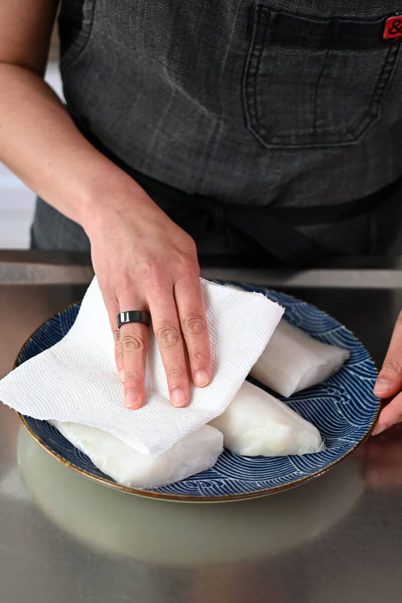 Patting raw fish filets with a paper towel before seasoning them with salt and pepper.