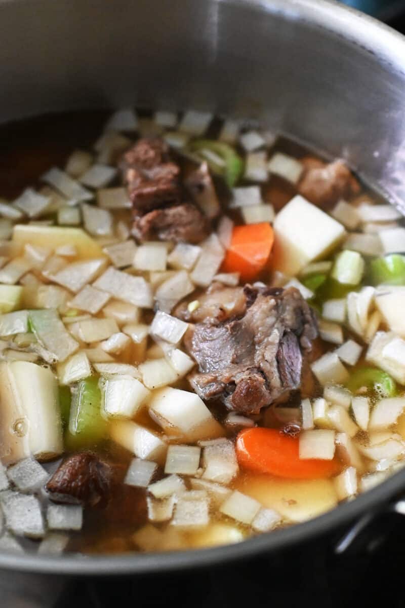 An overhead shot of oxtail soup and chopped vegetables simmering in a pot.