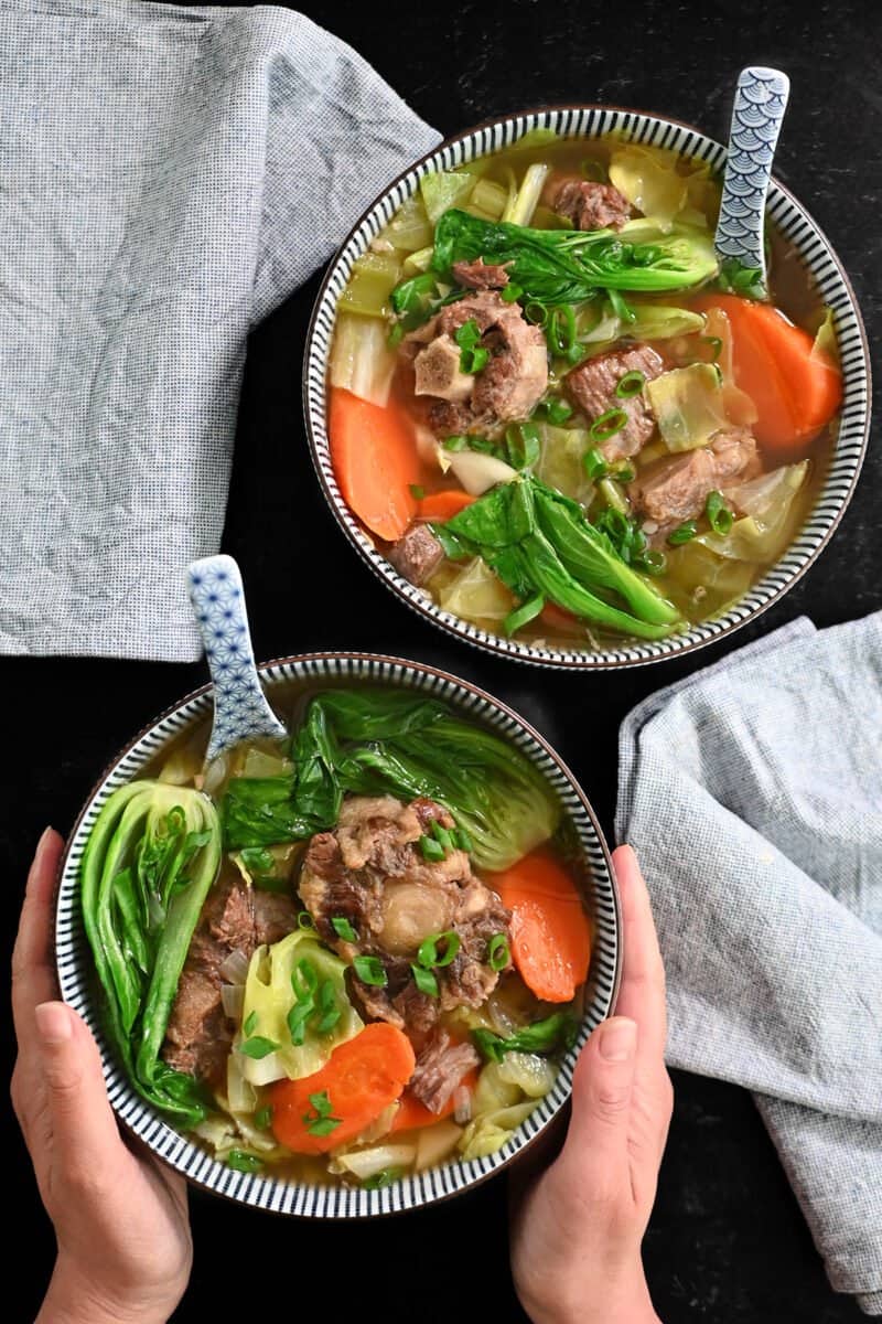 Two bowls of oxtail soup and vegetables.