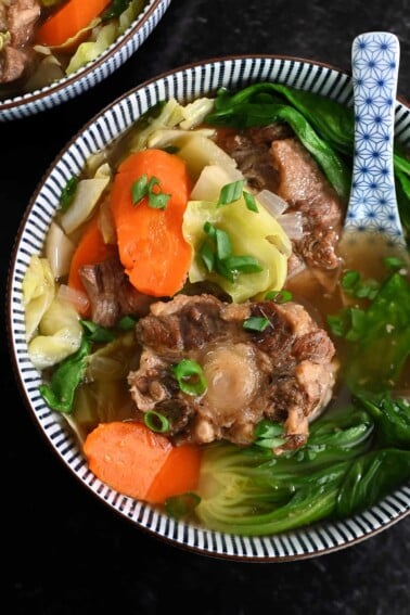 An overhead shot of a bowl filled with oxtail soup and vegetables.