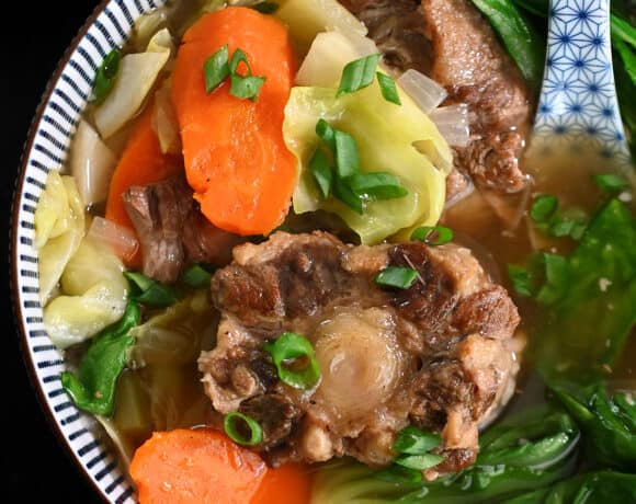 An overhead shot of a bowl filled with oxtail soup and vegetables.