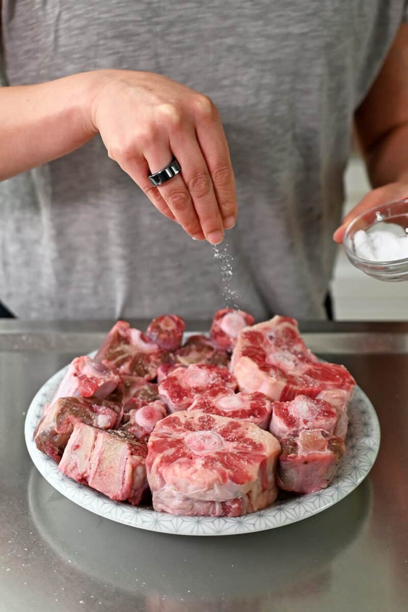 Sprinkling salt on a plate filed with raw oxtails to make oxtail soup