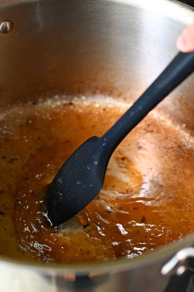 A black silicone spatula is scraping the browned bits off the bottom of a stockpot with some water.