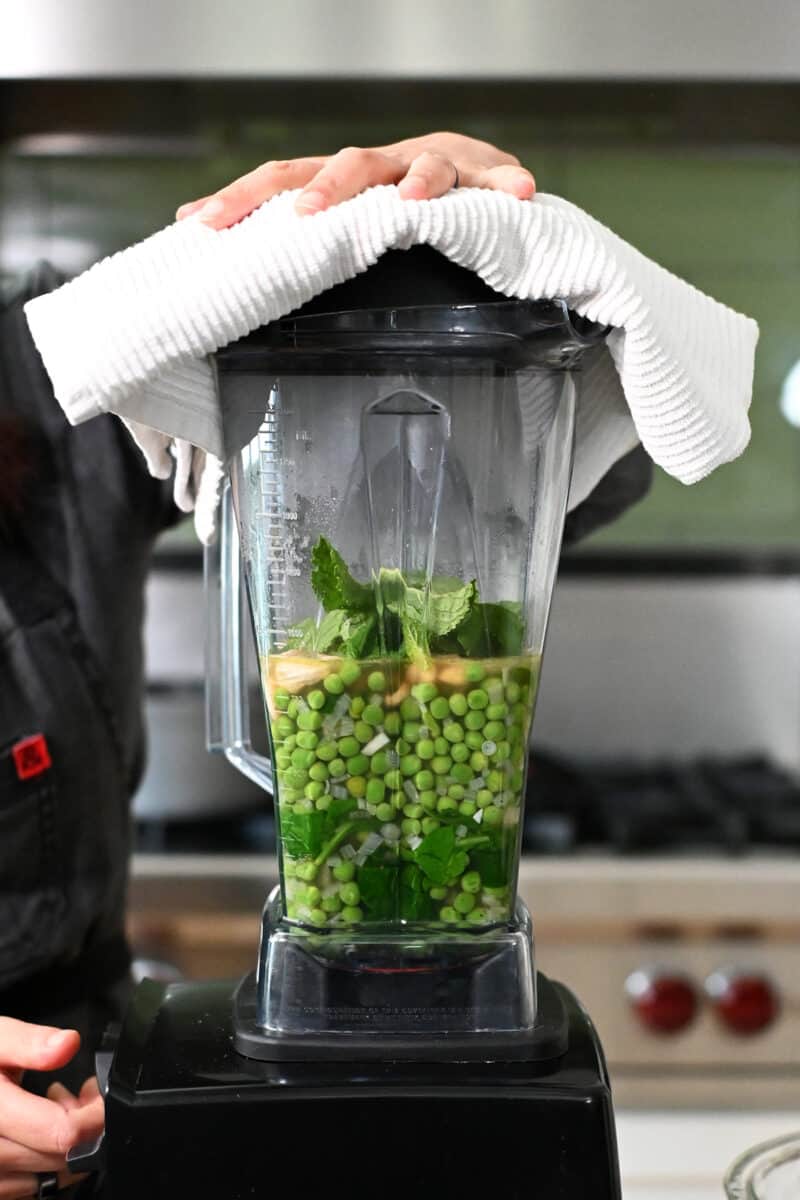 Side view of a Vitamix blender filled with pea soup ingredients.