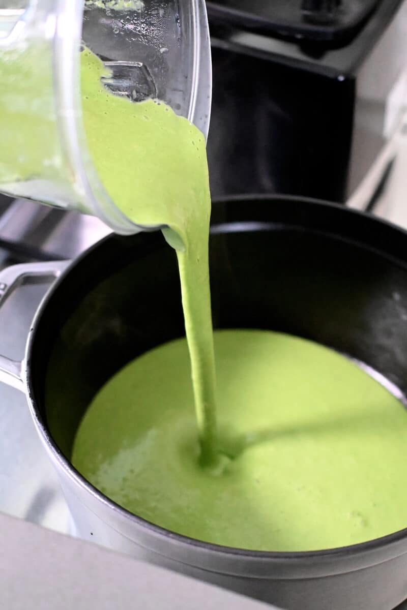 Pouring pea soup from a Vitamix blender to a gray dutch oven