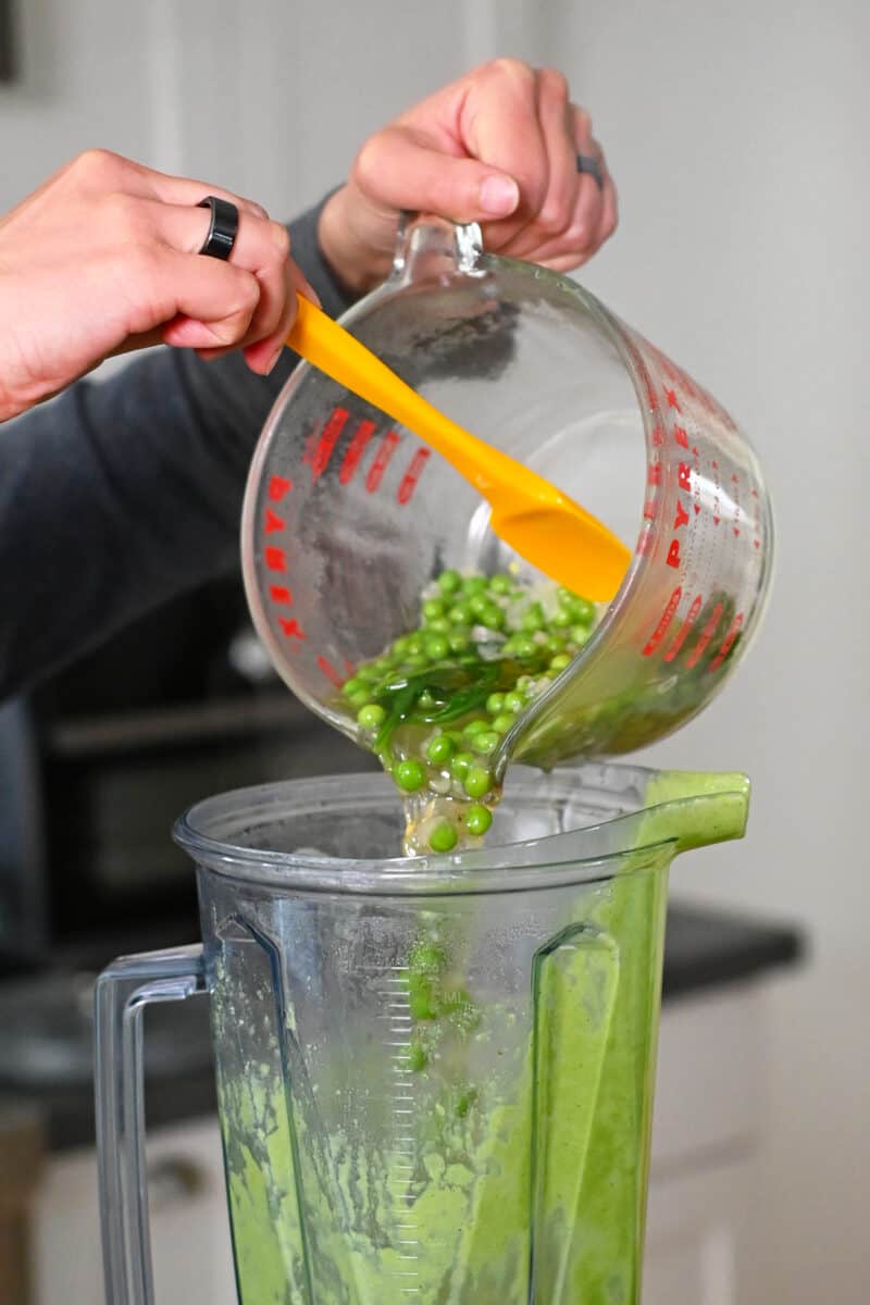 Transferring pea soup ingredients from a liquid measuring cup into a Vitamix blender.