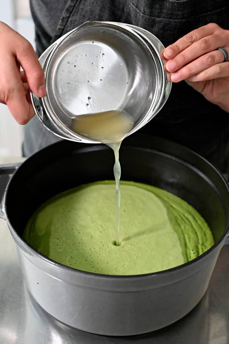 Pouring fresh lemon juice into a pot of smooth pea soup