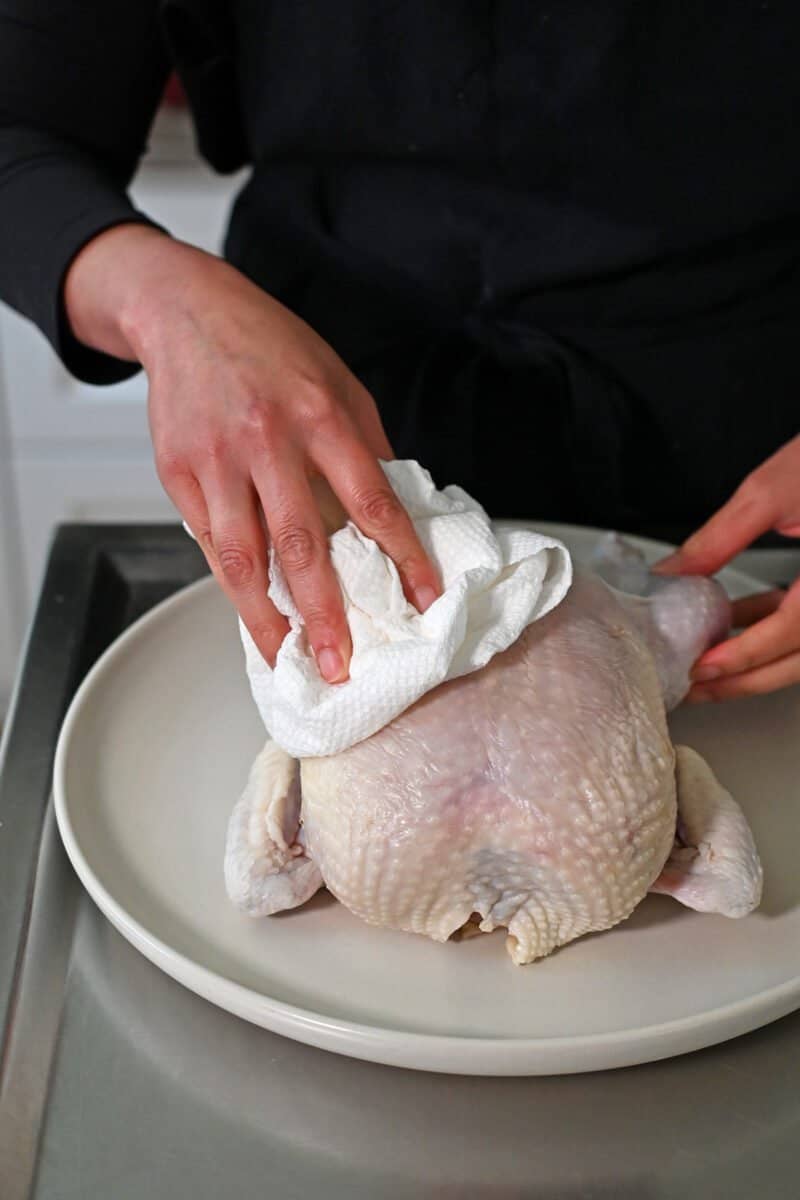 A whole raw chicken is being blotted dry with paper towels
