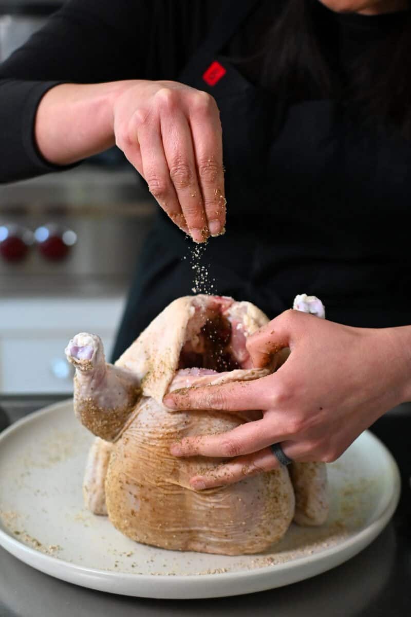 Sprinkling seasoning in the cavity of a raw chicken