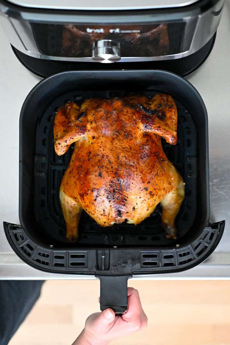 An open air fryer showing a golden brown whole chicken, breast side down