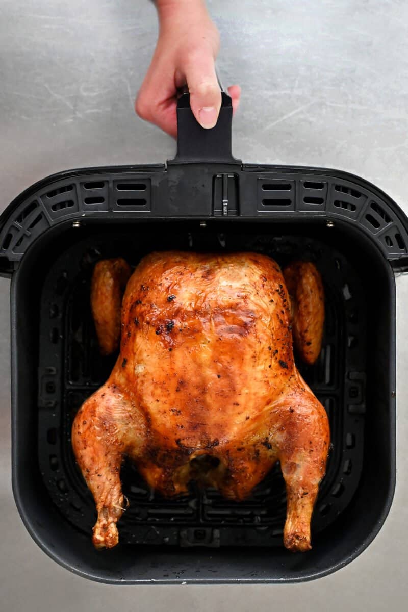 An overhead shot of an air fryer basket with a fully cooked whole chicken 