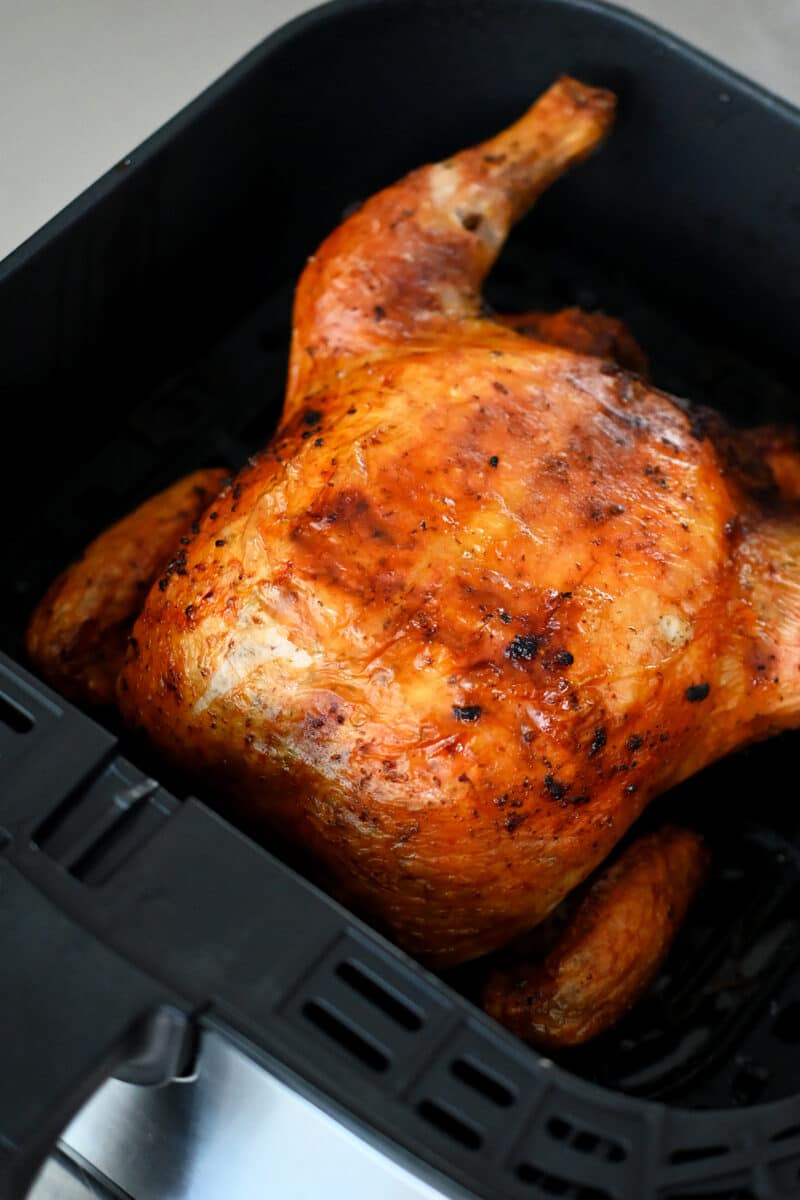 A side shot of an air fryer basket filled with a golden brown rotisserie-style whole chicken