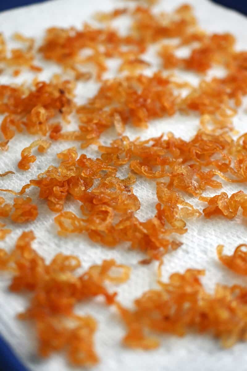 A closeup of a tray of crispy shallots draining on paper towels.