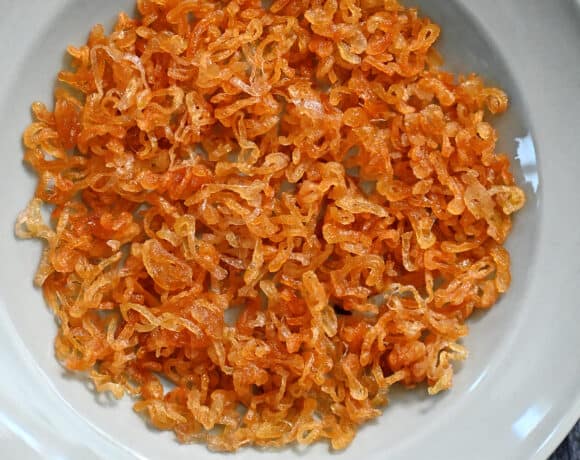 An overhead shot of a light blue plate filled with golden brown crispy shallots.