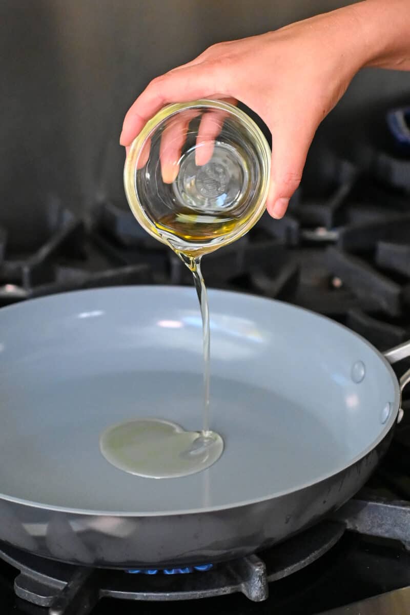 Adding avocado oil to a large skillet. 