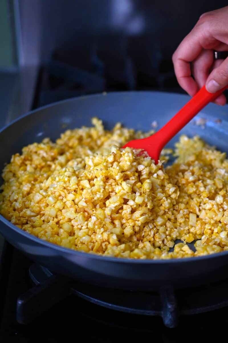 A skillet is filled with cauliflower rice coated with egg yolks.