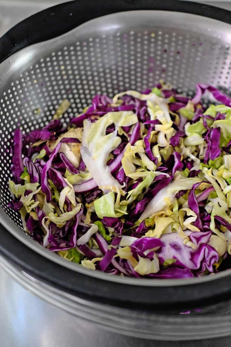 Shredded green and red cabbage that is wilted in a colander.