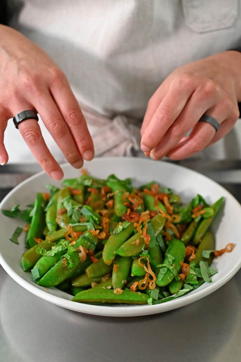 Scattering crispy shallots to a plate of stir fried sugar snap peas.