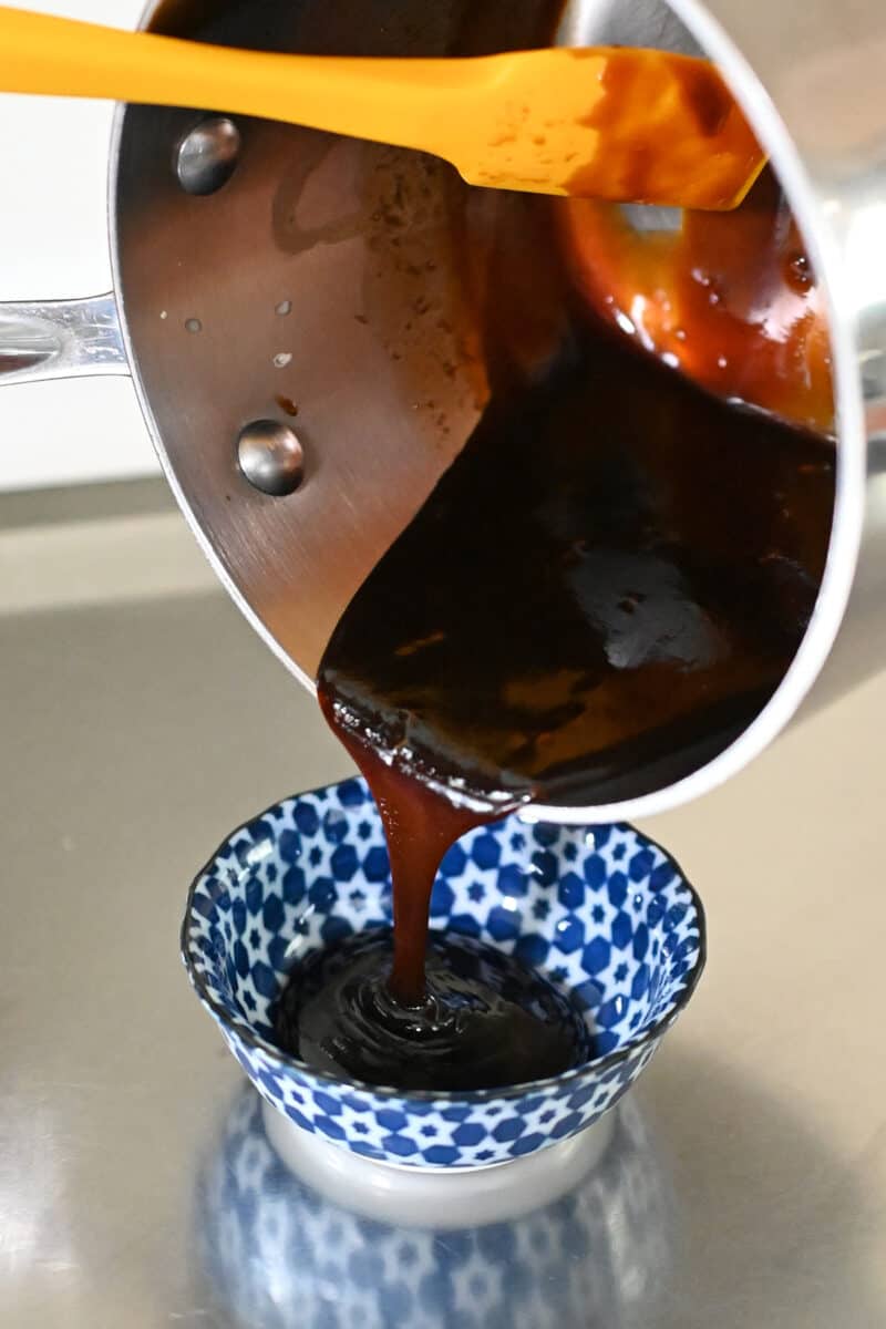 Pouring honey sriracha sauce from a saucepan into a small bowl.