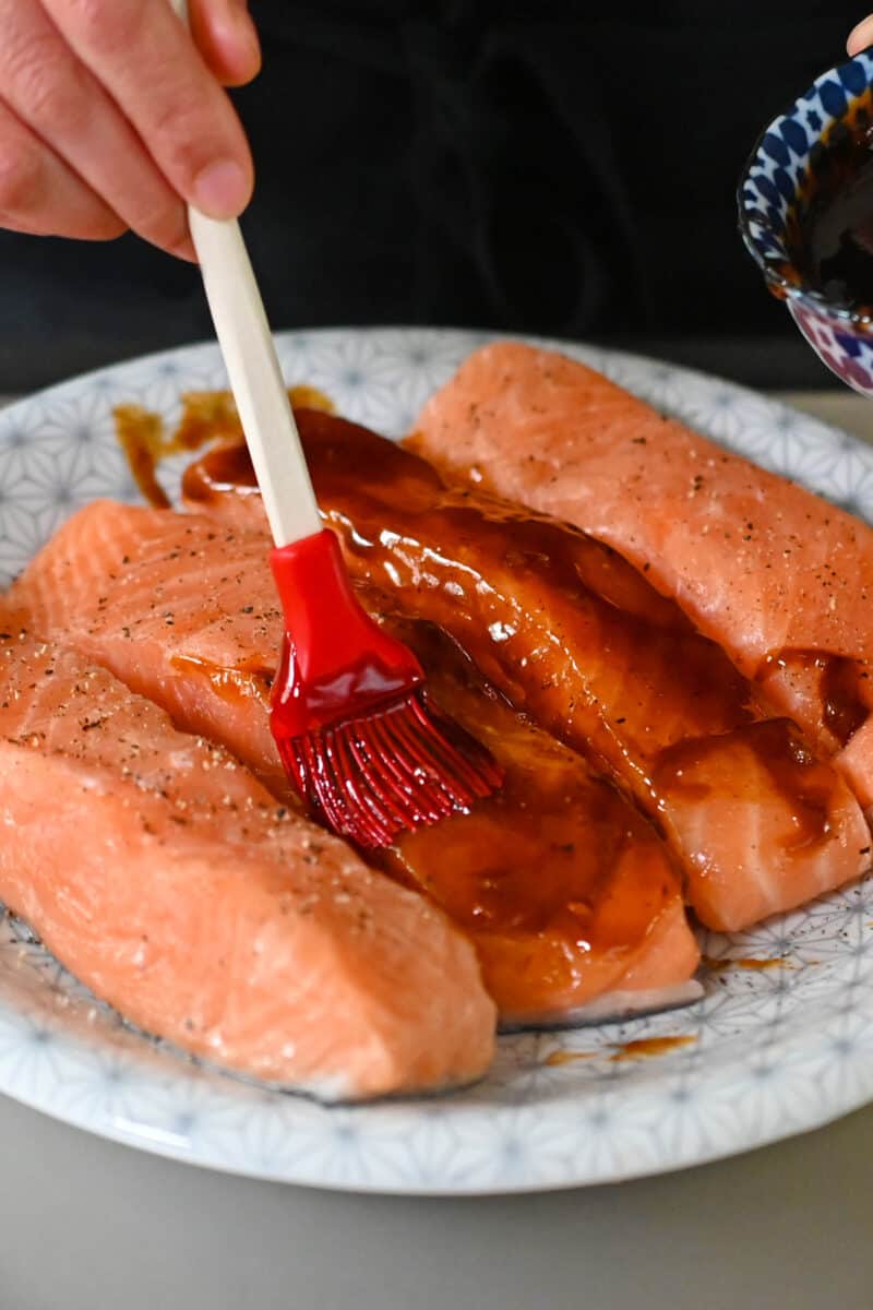 The raw salmon fillets are brushed with the honey sriracha sauce with a silicone brush.