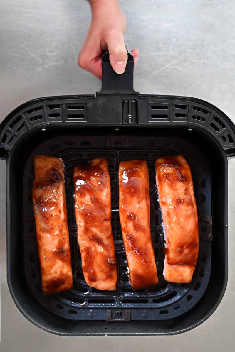 An overhead shot of an open air fryer with four salmon fillets inside with honey sriracha glaze.