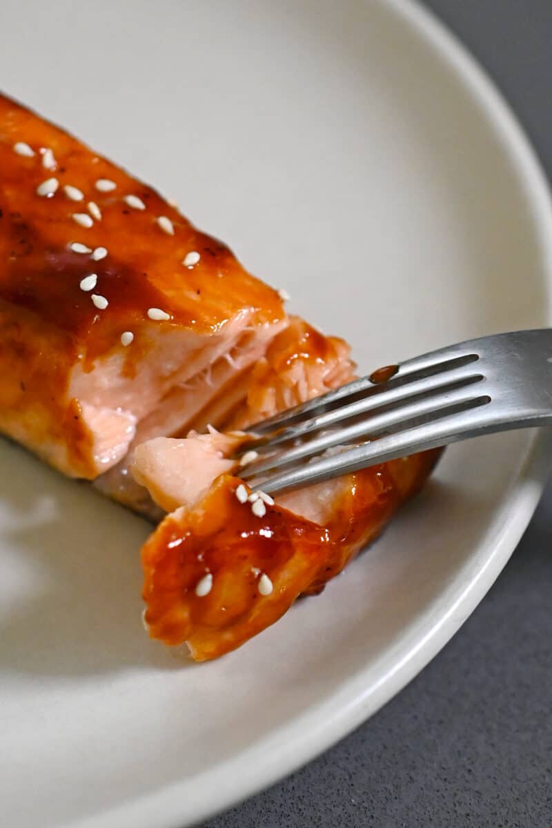 A fork is showing that the air fryer salmon with honey sriracha glaze is moist and just cooked through.
