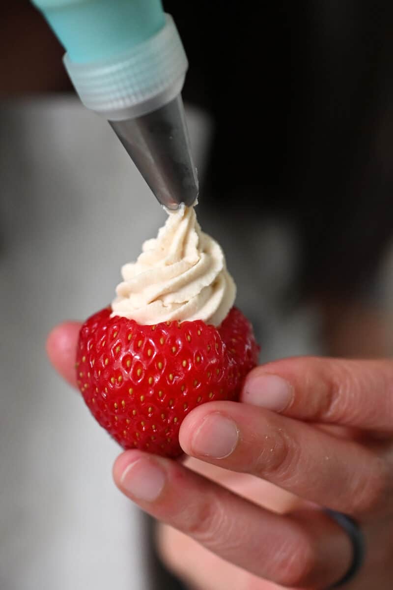Piping cheesecake filling into a hollowed out strawberry.