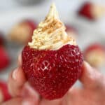 A hand is holding up a paleo and vegan cheesecake stuffed strawberry topped with gluten-free cookie crumbs.
