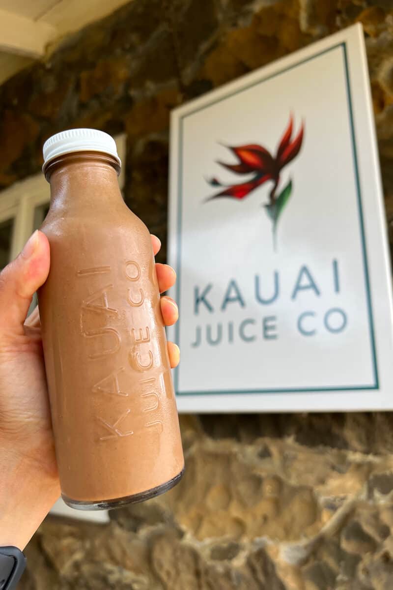 A hand is holding up a bottle of Black Pearl in front of a Kauai Juice Co sign.