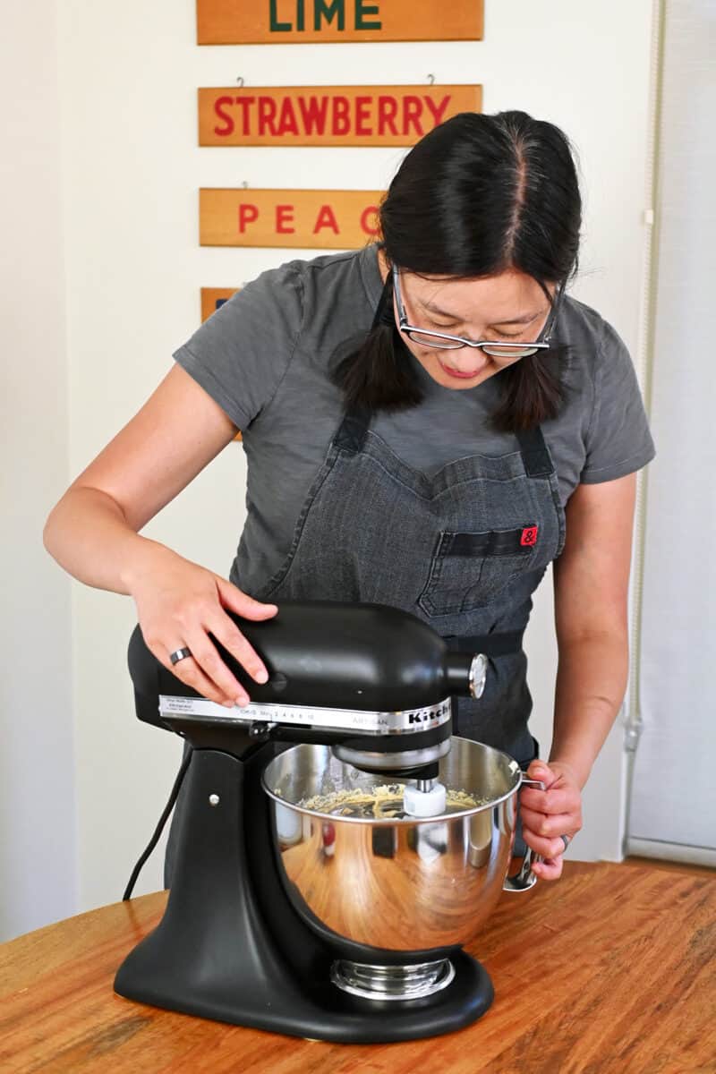An Asian woman is making paleo peach cake batter in a black Kitchen mixer.