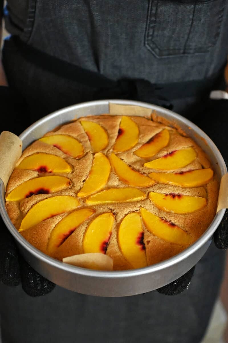 Removing a paleo and gluten free peach cake out of an oven.