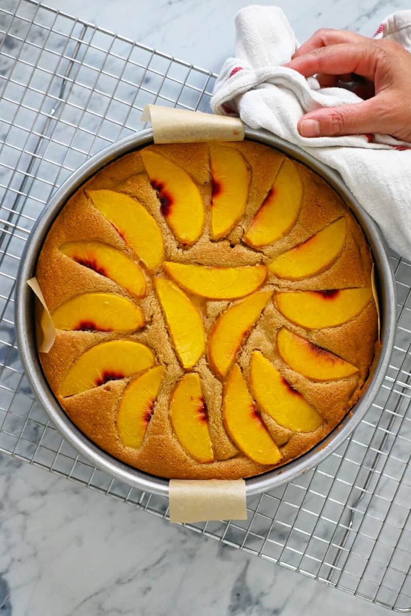 A golden brown freshly baked peach cake is cooling on a wire rack.