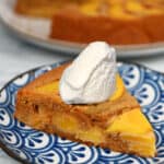A slice of paleo peach cake on a blue plate with a dollop of whipped coconut cream on top.