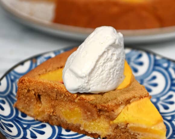 A slice of paleo peach cake on a blue plate with a dollop of whipped coconut cream on top.
