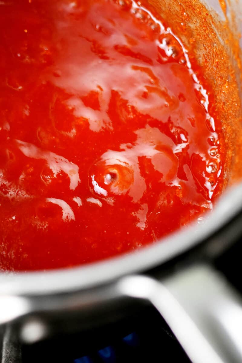 A bubbling red Whole30 barbecue sauce in a stainless steel saucepan.