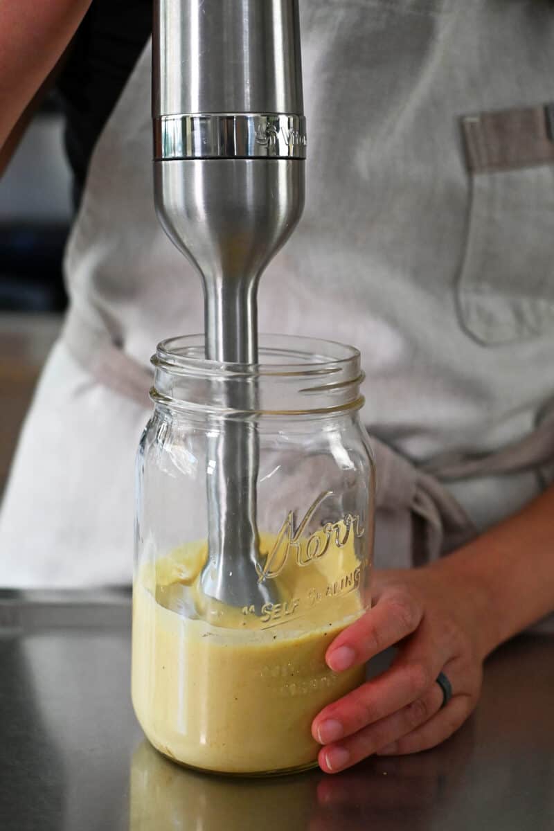 An immersion blender is blending dairy free caesar dressing in a large mason jar.
