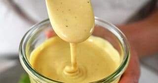 A spoon dipping into a jar of dairy-free Caesar Dressing.