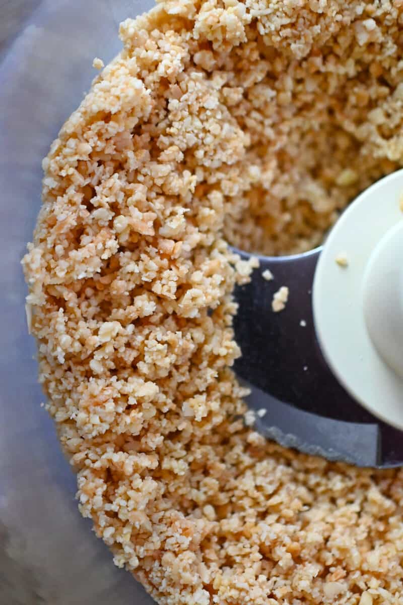 An overhead shot of a food processor filled with chunky almond and coconut flour.