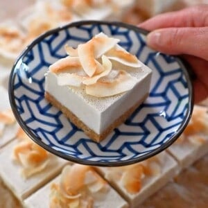 A hand holding a blue and white plate with a coconut cream bar on top.