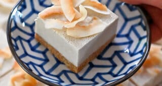 A hand holding a blue and white plate with a coconut cream bar on top.